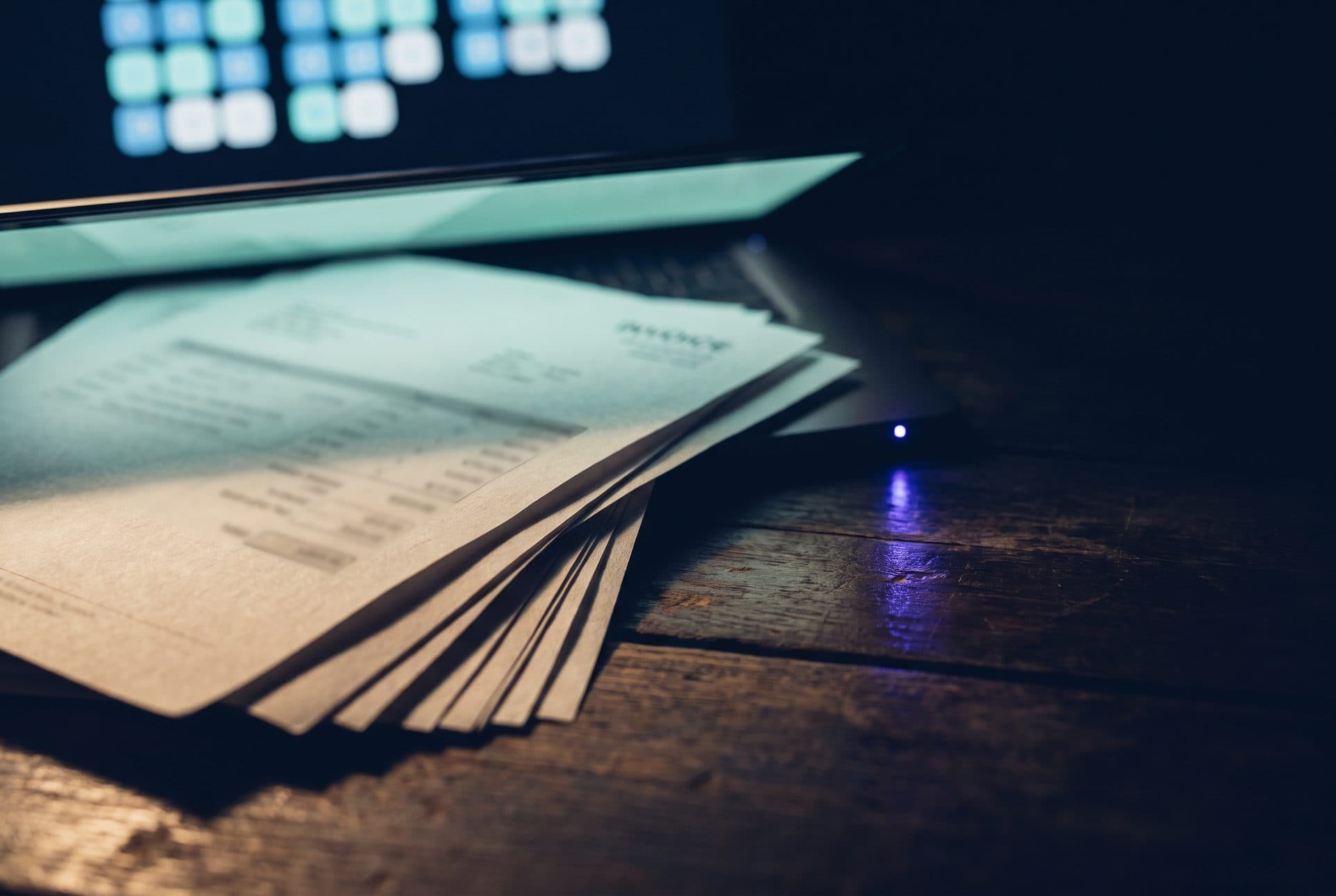 Facturas de proveedor en papel iluminadas por la pantalla del ERP, automatización de facturas en una pyme